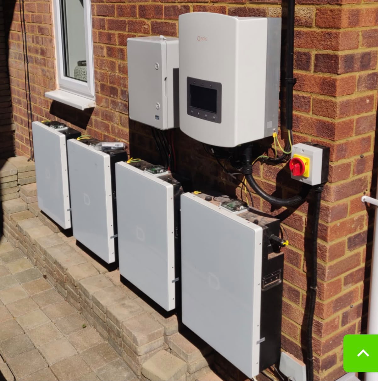 Four-unit home battery bank with hybrid inverter on a red-brick exterior wall