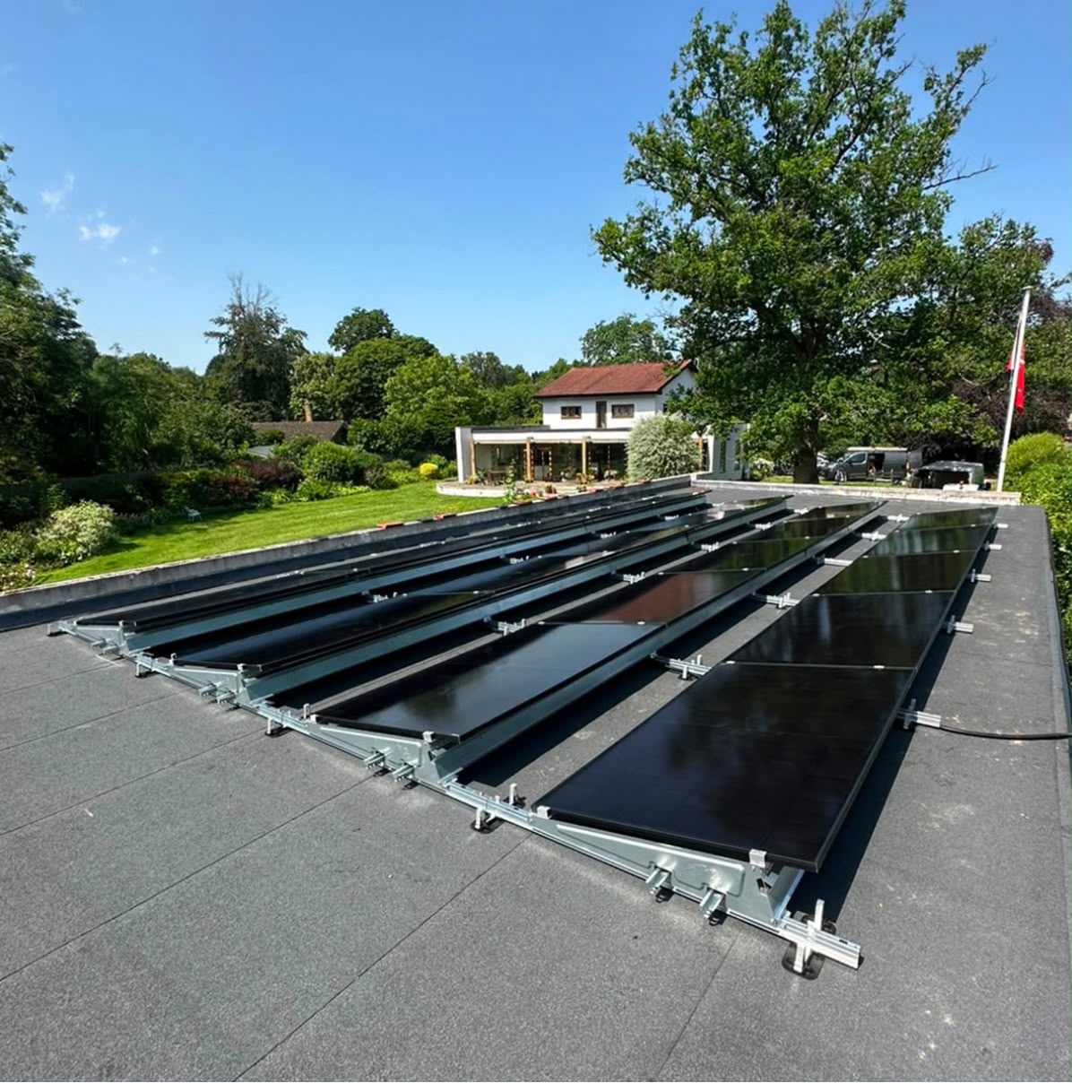 Ballasted flat-roof solar array on tilt frames overlooking a garden