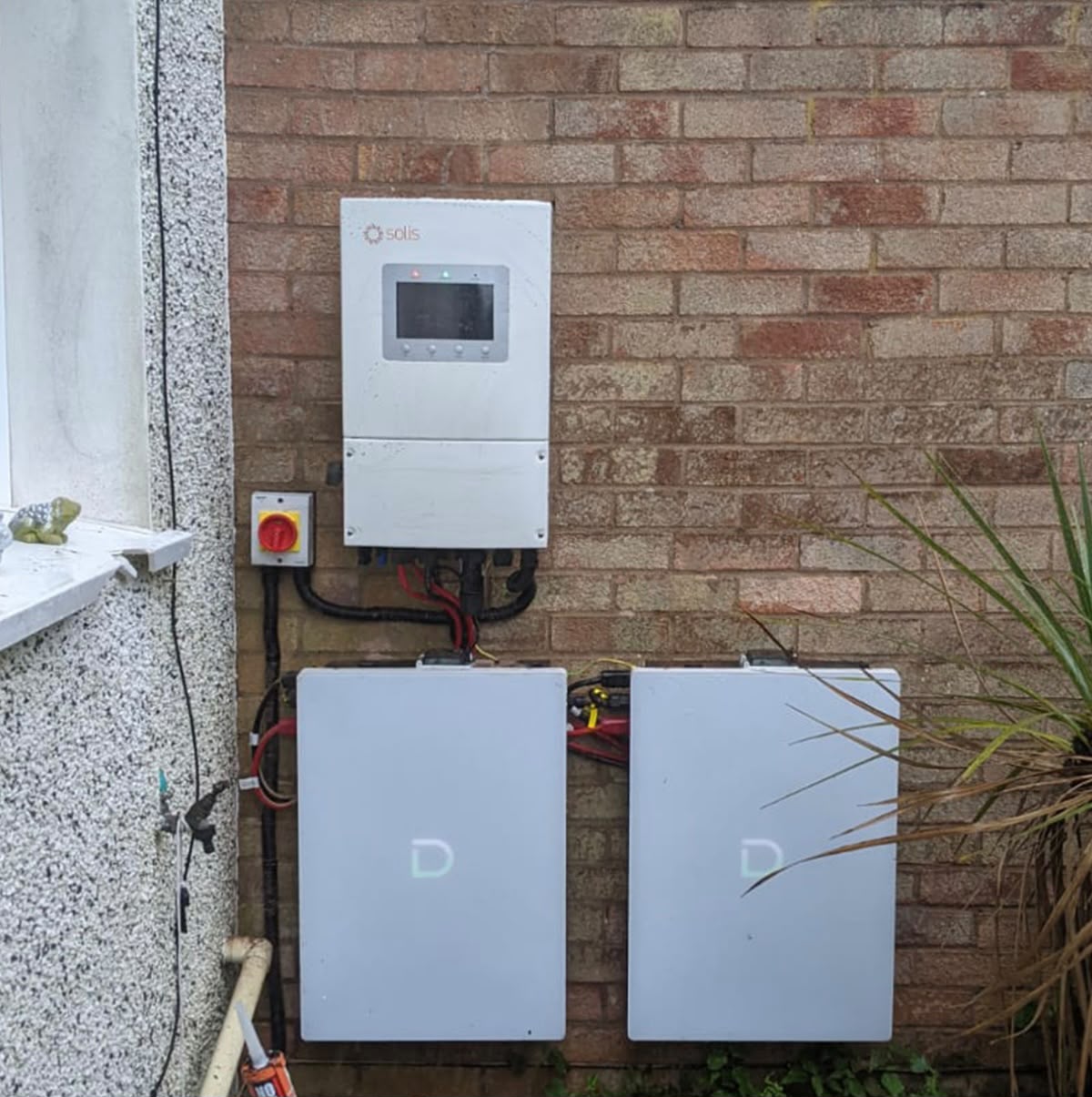 Solis inverter with two stacked home battery units installed outdoors on a brick wall