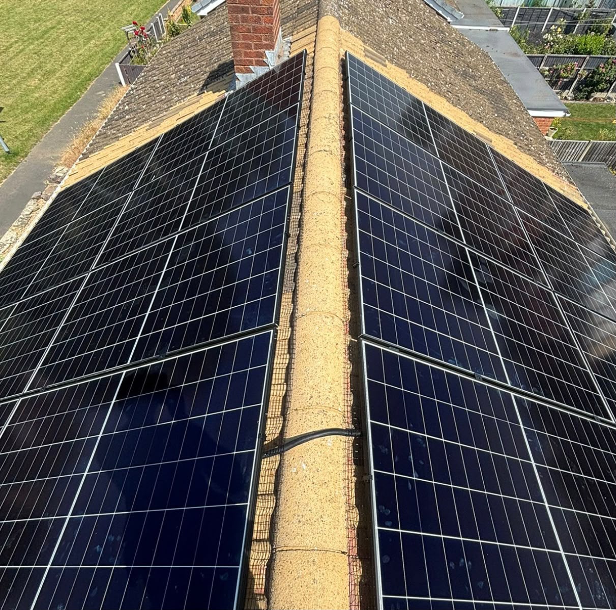 Twin black solar panel arrays installed either side of a chimney on a pitched tiled roof in Devon