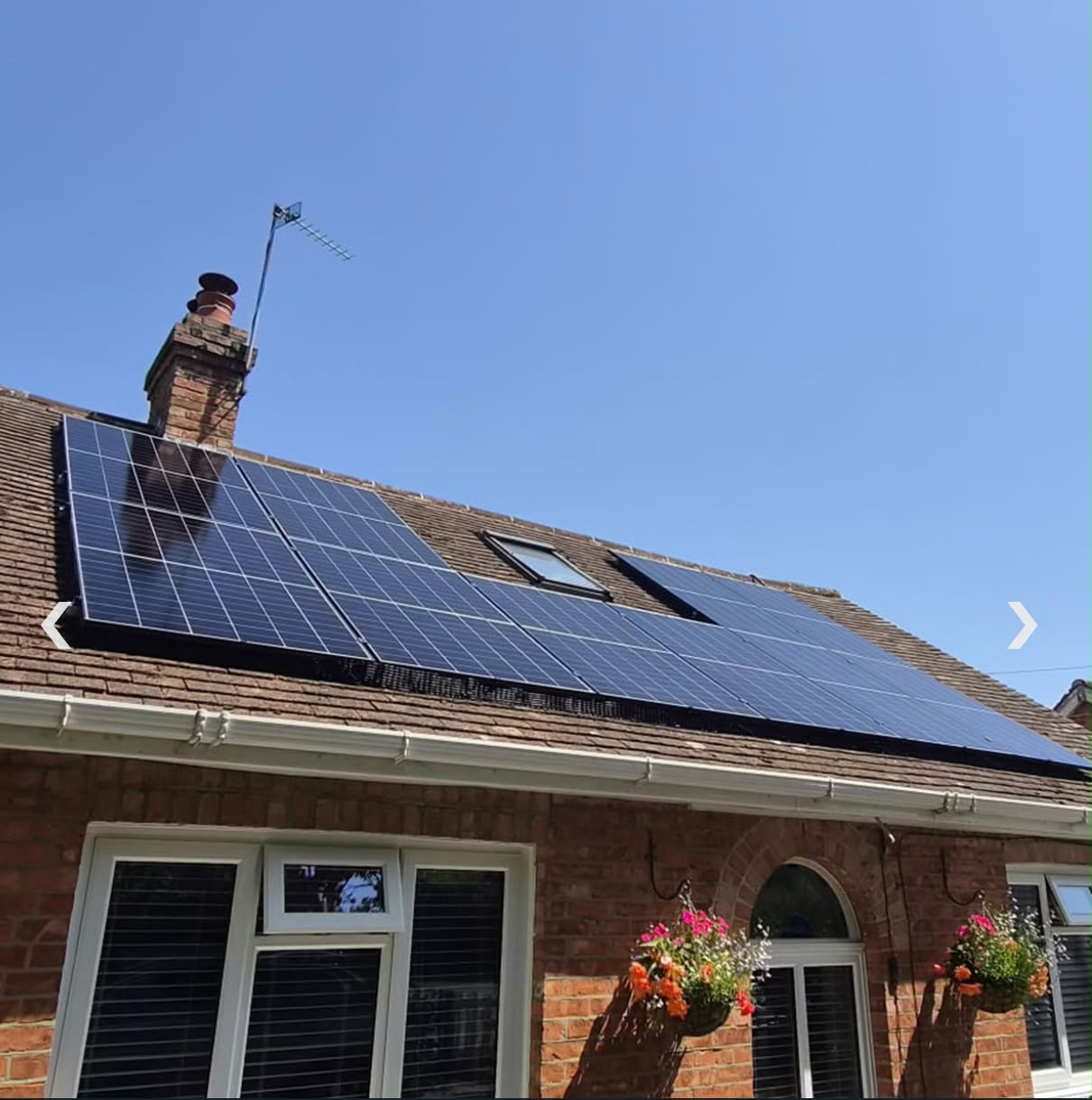 Solar panel array installed on a red-tile pitched roof beside a brick chimney