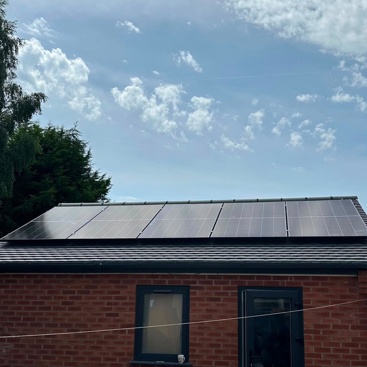 Row of solar panels along a black-tile pitched roof on a red-brick outbuilding