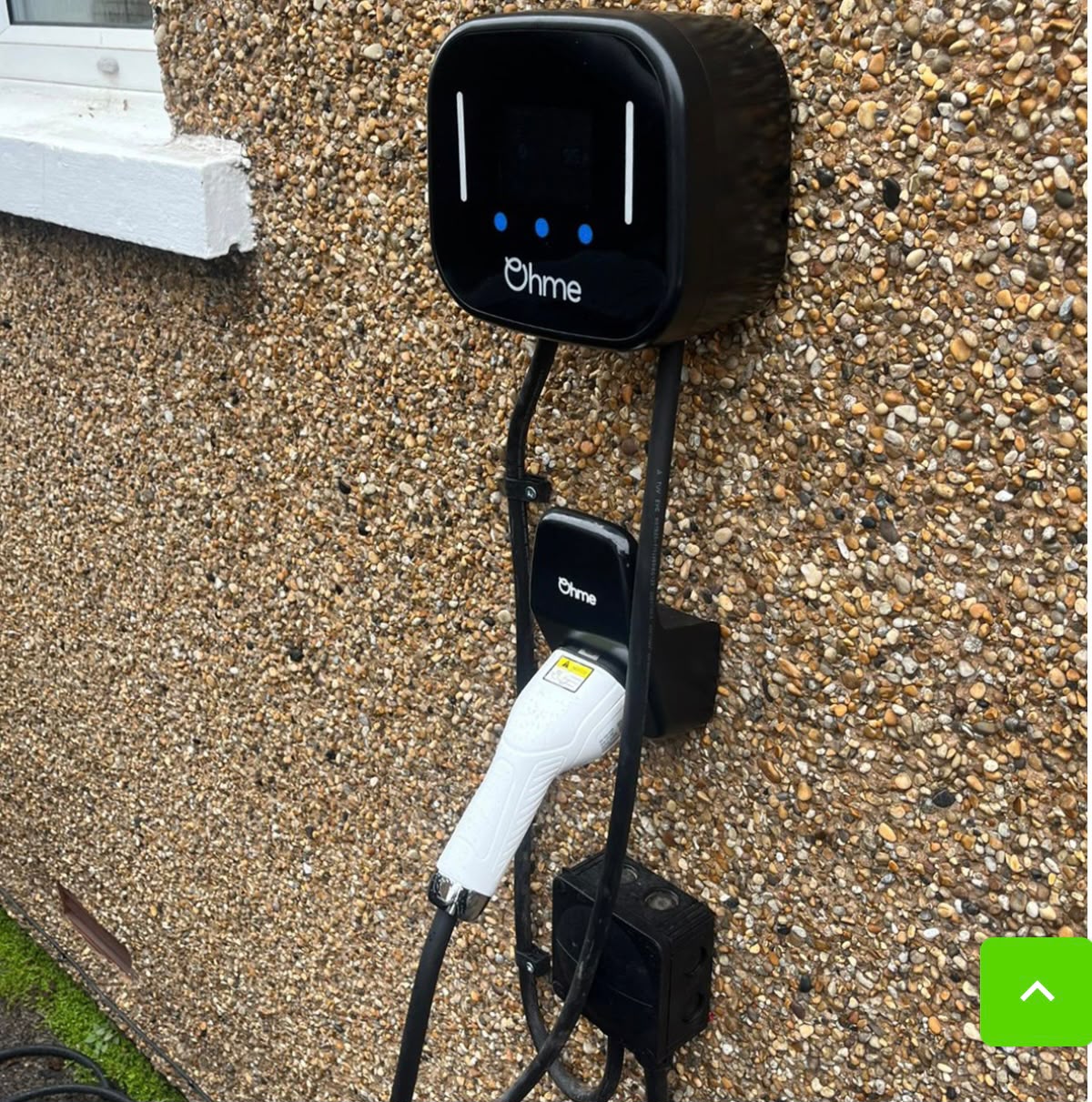 Ohme home EV charger installed on a pebbledash wall with EV connector holstered