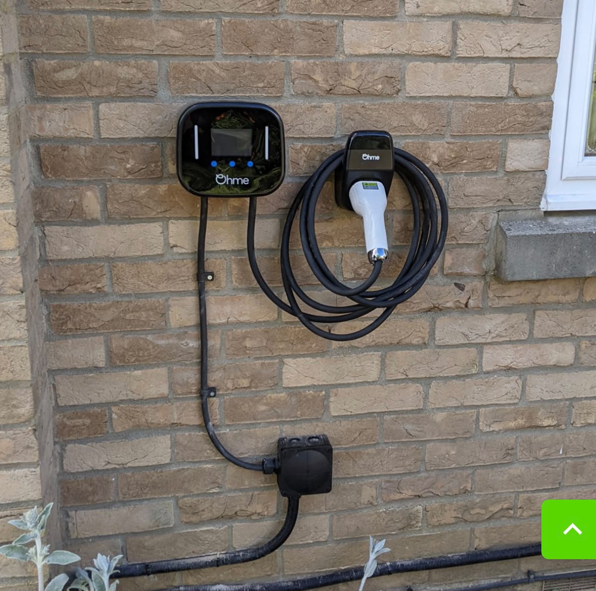 Ohme home EV charger installed on a light-brick exterior wall with cable holster