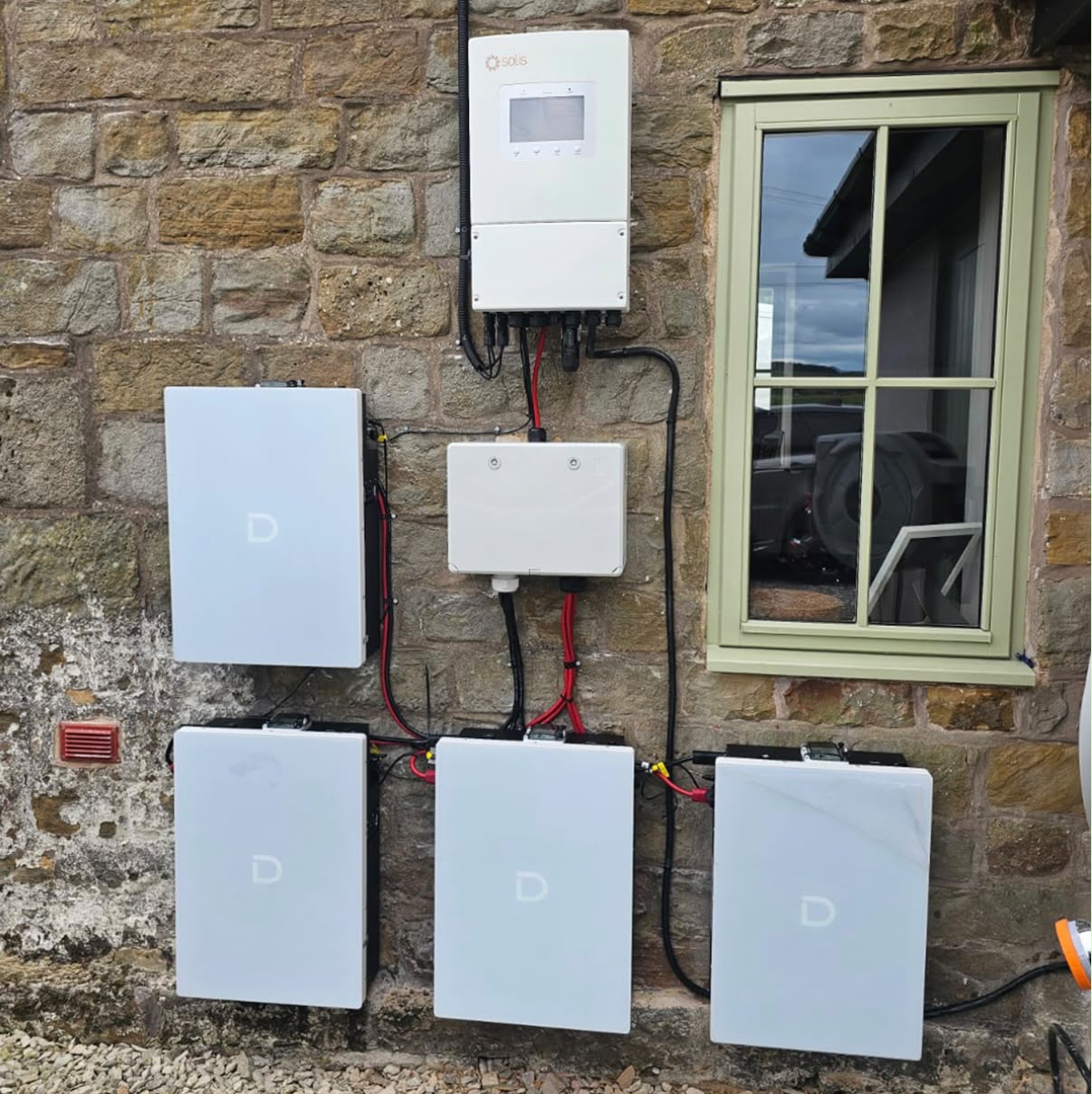 Six-unit home battery storage bank with hybrid inverter on a stone cottage wall